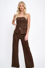 Conjunto de dos piezas confeccionado en tela agamuzada. Incluye un top strapless con cierre frontal de botones y bolsillos decorativos, y un pantalón de corte recto y tiro alto.