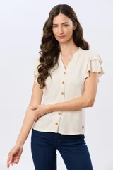 Camisa de lino y viscosa color beige, con cuello mao, escote en V y botones frontales de madera. Presenta mangas cortas con volados delicados.