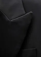 Chaqueta de corte sastre en mezcla de lana, color negro, con solapas satinadas, cierre frontal de un botón y bolsillos con solapa. Presenta mangas largas con detalle de tejido semitransparente en los puños.