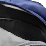 Mochila de diseño minimalista en color azul, confeccionada en material textil. Cuenta con un compartimento principal con cierre de doble cursor, un bolsillo frontal con solapa y cierre de hebilla metálica, y asa superior reforzada.