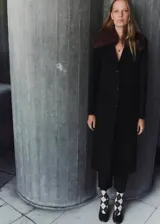 Abrigo largo de corte recto confeccionado en mezcla de lana, con cuello de solapa y cuello de pelo sintético extraíble. Presenta cierre frontal con botones, mangas largas y dos bolsillos con solapa en la parte delantera.