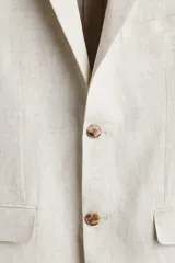 Blazer de lino liviano color beige, con solapas de muesca finas, botonadura sencilla de un botón, bolsillos con solapa en el frente y bolsillo superior ojal.