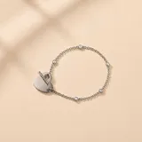 Pulsera de plata con cierre tipo T-bar, dijes de circonias engastadas a lo largo de la cadena y un dije colgante en forma de corazón.