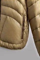 Campera puffer color beige con cuello alto, cierre frontal con cremallera y bolsillos laterales con cierre. Diseño acolchado horizontal.