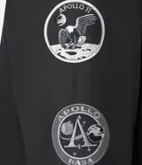Campera tipo bomber color negro, con cierre frontal, cuello, puños y ruedo acanalados. Presenta parches bordados en el pecho con la bandera de Estados Unidos y el logo de la NASA, además de un bolsillo utilitario con cierre en la manga izquierda.