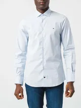 Camisa Tommy Hilfiger de algodón Oxford celeste con microestampado. Tiene corte regular, cuello abotonado, mangas largas con puños abotonados y logo bordado en el pecho.