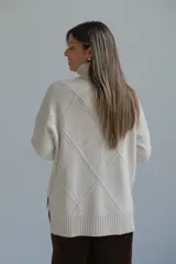 Polerón de cuello alto con diseño de rombos tejidos en relieve, mangas largas con puños acanalados y ruedo asimétrico con aberturas laterales.