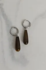 Aros tipo argolla de acero quirúrgico con dije colgante en forma de gota de piedra natural en tono marrón.