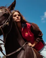 Camisa de pana de corte amplio con diseño color block, cuello camisero y mangas largas. Presenta bordados decorativos en el frente que incluyen un sol, un caballo y una bandera.