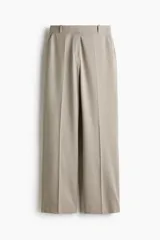 Pantalón sastrero de sarga color beige, con cintura clásica, trabillas para cinto y cierre frontal oculto. Presenta bolsillos laterales al bies, pliegues frontales y piernas rectas con raya marcada.