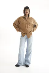 Camisa color marrón claro de pana, corte oversize, con cuello clásico, cierre frontal con botones, dos bolsillos con solapa en el pecho y mangas largas con puños abotonados.