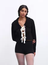 Chaqueta corta tejida en lana y algodón de color negro, con cuello polo y cierre frontal con lazos blancos.