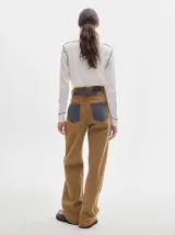 Pantalón jean de tiro alto y corte pinzado, con perneras de caída suelta y levemente anchas en el bajo. Posee pasador con hebilla en la parte trasera.