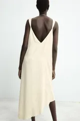 Vestido midi de color beige con diseño jacquard sutil. Presenta un escote en pico pronunciado, tirantes anchos y un bajo con acabado asimétrico.