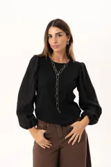 Blusa negra de tejido acanalado con mangas largas abullonadas de textura arrugada y puños elásticos.