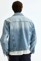Campera trucker de denim de algodón rígido en color celeste con lavado claro, cuello camisero, cierre frontal de botones metálicos, bolsillos con solapa en el pecho y bolsillos laterales.