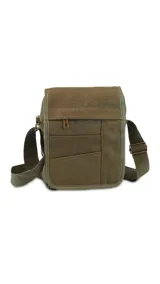 Morral de tela canvas color verde oliva, con tapa, apertura superior y cierre. Tiene bolsillos en la tapa al frente, uno con cierre, y un bolsillo auxiliar también al frente con cierre bajo la tapa. Incluye un bolsillo con cierre atrás y correa larga regulable.