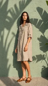 Vestido camisero midi de lino color beige, de calce relajado, con cuello clásico, cierre frontal parcial con botones, mangas 3/4 regulables y bolsillos delanteros.