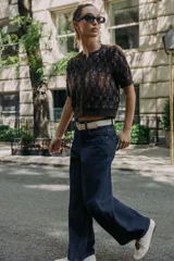 Chaqueta de punto texturizado con cuello redondo y manga corta. Presenta un patrón de rombos en tonos marrón oscuro, negro y blanco. Cierre frontal con botones oscuros.