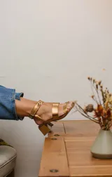 Sandalias negras de cuero con dos tiras horizontales sobre el pie y pulsera al tobillo con ojalillos y tachas. Taco cuadrado de 5 cm.