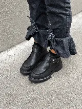 Bota corta tipo borcego de cuero negro, con suela track liviana y detalle de tira con hebilla metálica en el tobillo.