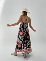 Vestido largo de algodón con estampado floral en tonos rojo, blanco y marrón sobre fondo negro. Tiene breteles finos cruzados en la espalda y corte imperio.