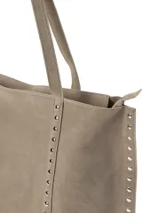 Bolso tipo shopper de gamuza en color gris, con detalles de tachuelas plateadas en los laterales. Cuenta con cierre superior y asas largas para llevar al hombro.