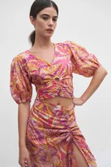 Blusa crop top rosada con estampado floral en tonos amarillos, naranjas y blancos, con escote en V, mangas abullonadas cortas y detalle de aro forrado en el centro del pecho con fruncidos.