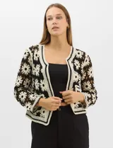 Cardigan abierto de tejido crochet con diseño de flores bicolores en negro y crema. Presenta mangas largas, frente abierto sin cierre y bolsillos frontales tipo parche. Posee terminaciones con franjas a contraste en escote, puños y ruedo.