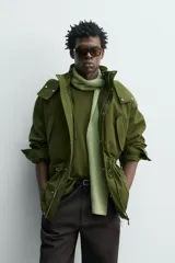 Parka técnica color verde militar de corte relaxed fit con cuello subido y capucha desmontable. Cuenta con bolsillos con solapa en el pecho y en la cadera, cintura ajustable con cordón y cierre frontal de cremallera oculta por solapa con botones a presión. Incluye un chaleco interior desmontable acolchado.
