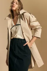 Top de tejido color beige claro, manga corta, escote en V con cierre frontal de botones y ribetes negros en el cuello y el borde del escote.