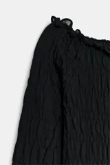Top negro de punto con textura de nido de abeja elástico, escote barco y mangas largas. Cuenta con detalles de volados en el cuello, los puños y el ruedo.