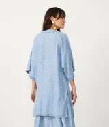 Kimono de lyocell (tejido tipo jean) color celeste claro con estampado repetitivo de pequeños peces blancos. Diseño de manga corta ancha y abertura frontal que se ajusta con un lazo fino en la cintura.