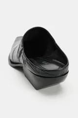 Zueco negro de piel con acabado grabado efecto cocodrilo, diseño destalonado, punta cuadrada y tacón ancho.