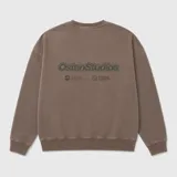 Buzo de cuello redondo en color marrón con efecto lavado, presenta un pequeño estampado gráfico en el pecho y una etiqueta decorativa en el ruedo.