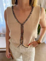 Chaleco tejido color arena con terminaciones en punto festón negro.