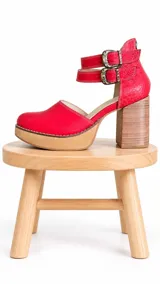 Zapatos de tacón alto de cuero rojo con plataforma y suela de madera, featuring doble correa con hebillas metálicas en el tobillo.