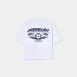 Camiseta blanca de corte "boxy fit" con estampado frontal en azul oscuro que incluye el texto "emestudios" y un diseño gráfico con estrellas y la palabra "MAD".