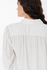 Camisa blanca de corte relajado, con cuello clásico, cierre frontal de botones y mangas largas amplias con puños ajustados.