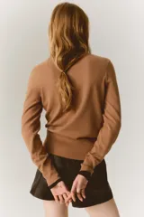 Buzo de punto fino en color tostado, con cuello en V acanalado y mangas largas con puños elastizados.
