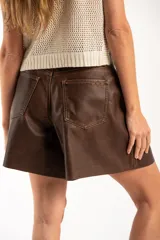 Bermuda de cuero vegano color marrón, con corte wide leg y tiro medio. Presenta diseño de cinco bolsillos y cierre frontal con botón metálico.