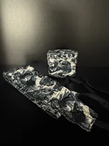 Par de muñequeras de tela color crema con estampado de dioses en negro.