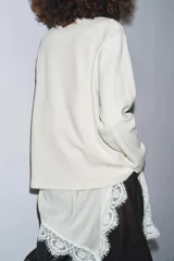 Camiseta color crudo de cuello redondo y manga larga, con detalle de aplicación de tejido lencero asimétrico a tono en el ruedo.