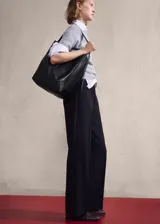 Bolso tipo shopper de cuero vacuno, color negro, con diseño minimalista, costura central vertical y asa de hombro ajustable con hebilla metálica.