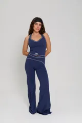 Conjunto deportivo compuesto por una musculosa de cuello halter con vivos en contraste y un pantalón de corte recto con cintura alta y detalles de costuras decorativas. Ambas piezas presentan el logo de la marca estampado.