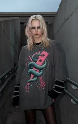 Remera de algodón color gris oscuro con efecto lavado, de corte holgado y manga corta. Presenta una estampa frontal detallada que muestra una serpiente entrelazada alrededor de una paleta de madera con corazones, rodeada por un diseño de alambre de púas.