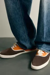 Zapatilla casual de hombre con diseño combinado en color naranja y marrón oscuro, con cordones y suela de goma en contraste.