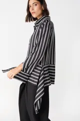 Camisa de corte holgado con estampado de cuadros en tonos marrones y beige. Presenta cuello clásico, cierre frontal con botones y mangas largas con aberturas laterales que permiten anudar la prenda en la cintura.