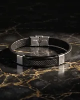 Pulsera de diseño masculino con banda de cuerina negra y placa central de acero con textura geométrica y detalles laterales en acero pulido.