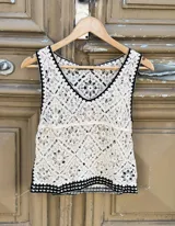 Blusa de crochet color beige con diseño calado, escote en V y terminaciones en color negro en el cuello, sisas y ruedo.